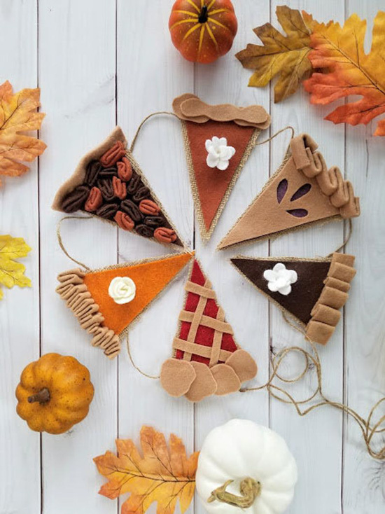 Felt bunting on twine each piece made to look like a different flavor of seasonal pie, and surrounded by autumn leaves and pumpkins. 