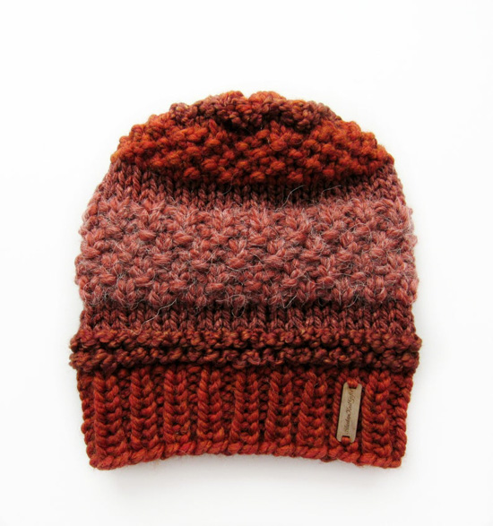 Multi-textured beanie in shades of burgundy and burnt orange with a small metal sewn on tag. 