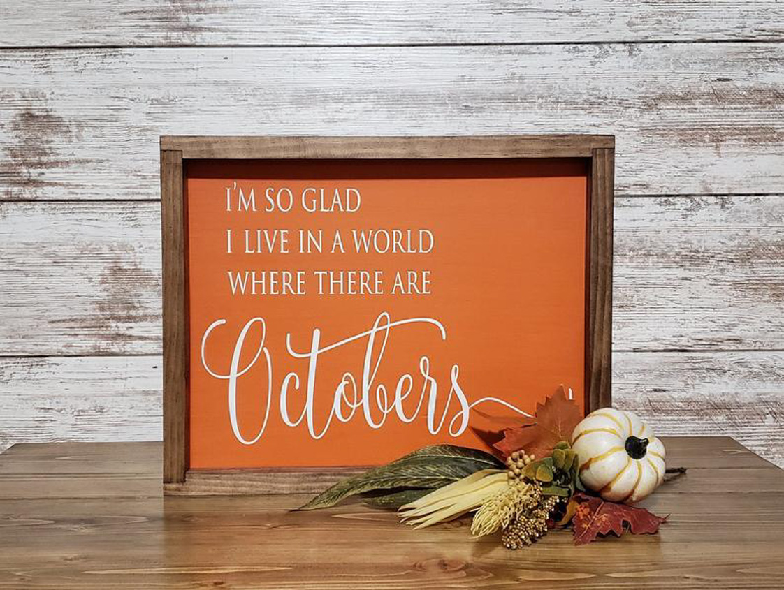 Rustic, farmhouse sign, wood frame and orange inlay that says, 'I'm so glad I live in a world where there are Octobers'.