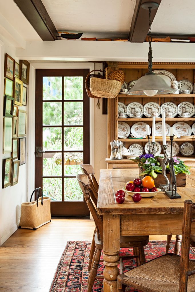 A rustic, farmhouse kitchen displaying a full china collection in a hutch and a substantial farmhouse table with wood and wicker chairs around it. 