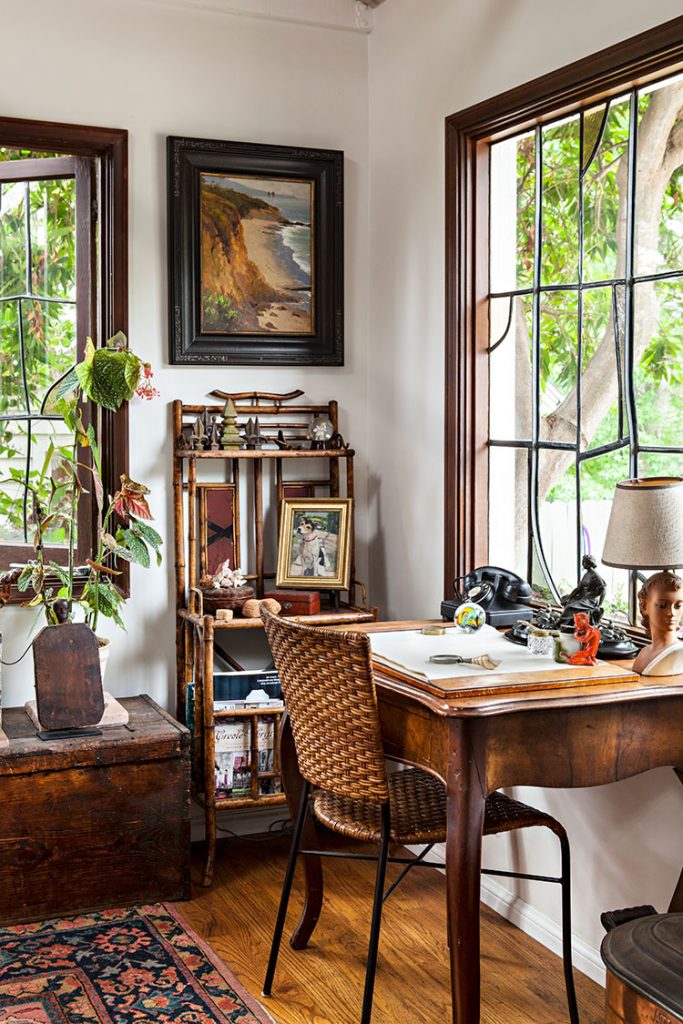 Rustic office with rich dark stained wood accents. Oriental rug, desk with wicker chair, vintage trunk and bamboo bookshelf all tucked into an office corner. 