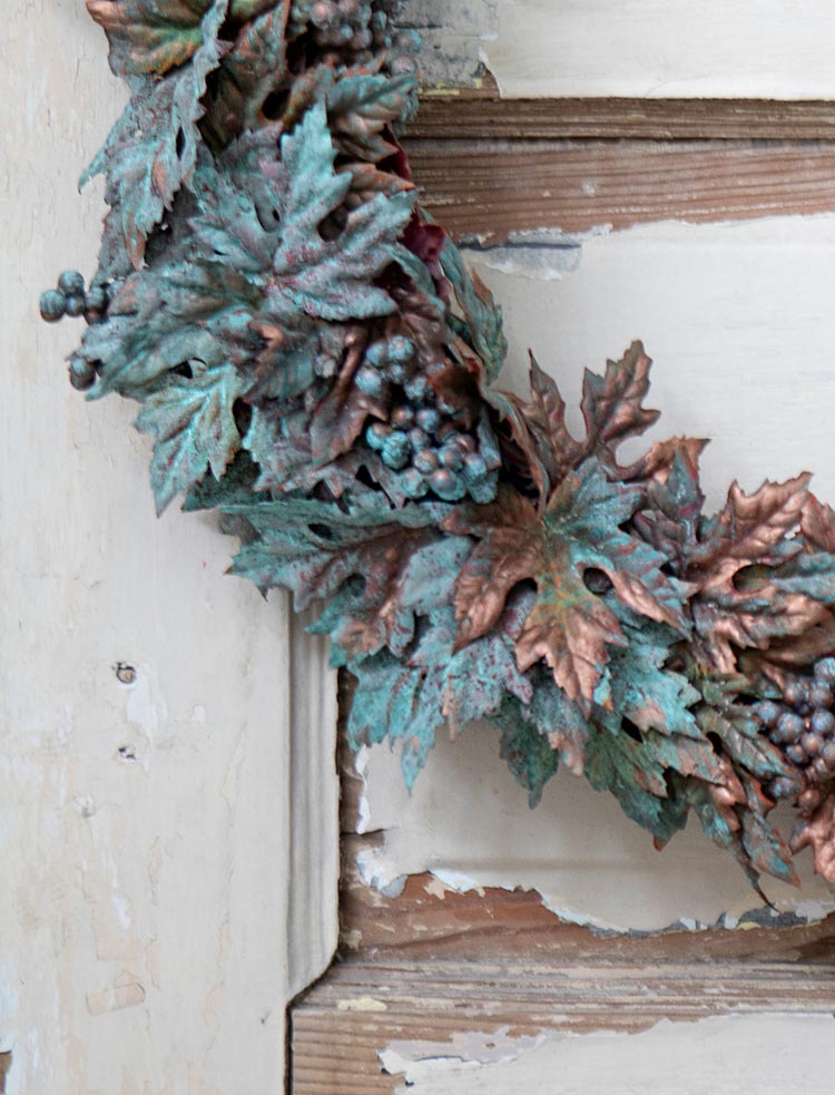 Close-up shot of a copper patina fall wreath on a door with white chipped paint