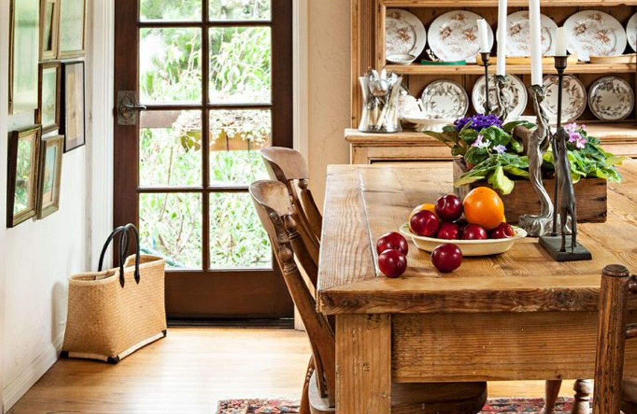 A rustic, farmhouse kitchen displaying a full china collection in a hutch and a substantial farmhouse table with wood and wicker chairs around it.