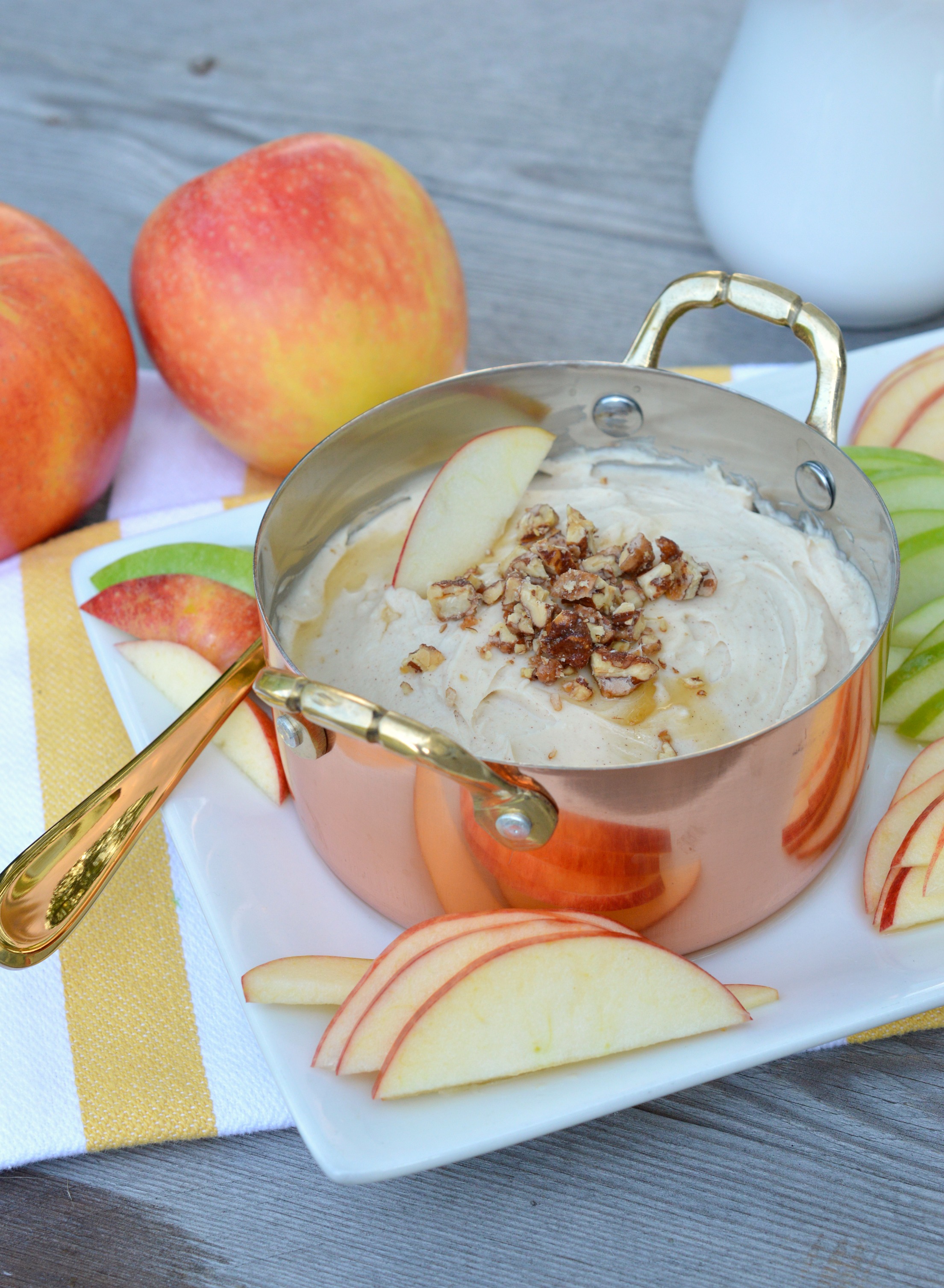 Pan filled with caramel apple cream cheese dip on a white tray and surrounded by green and red apple slices.