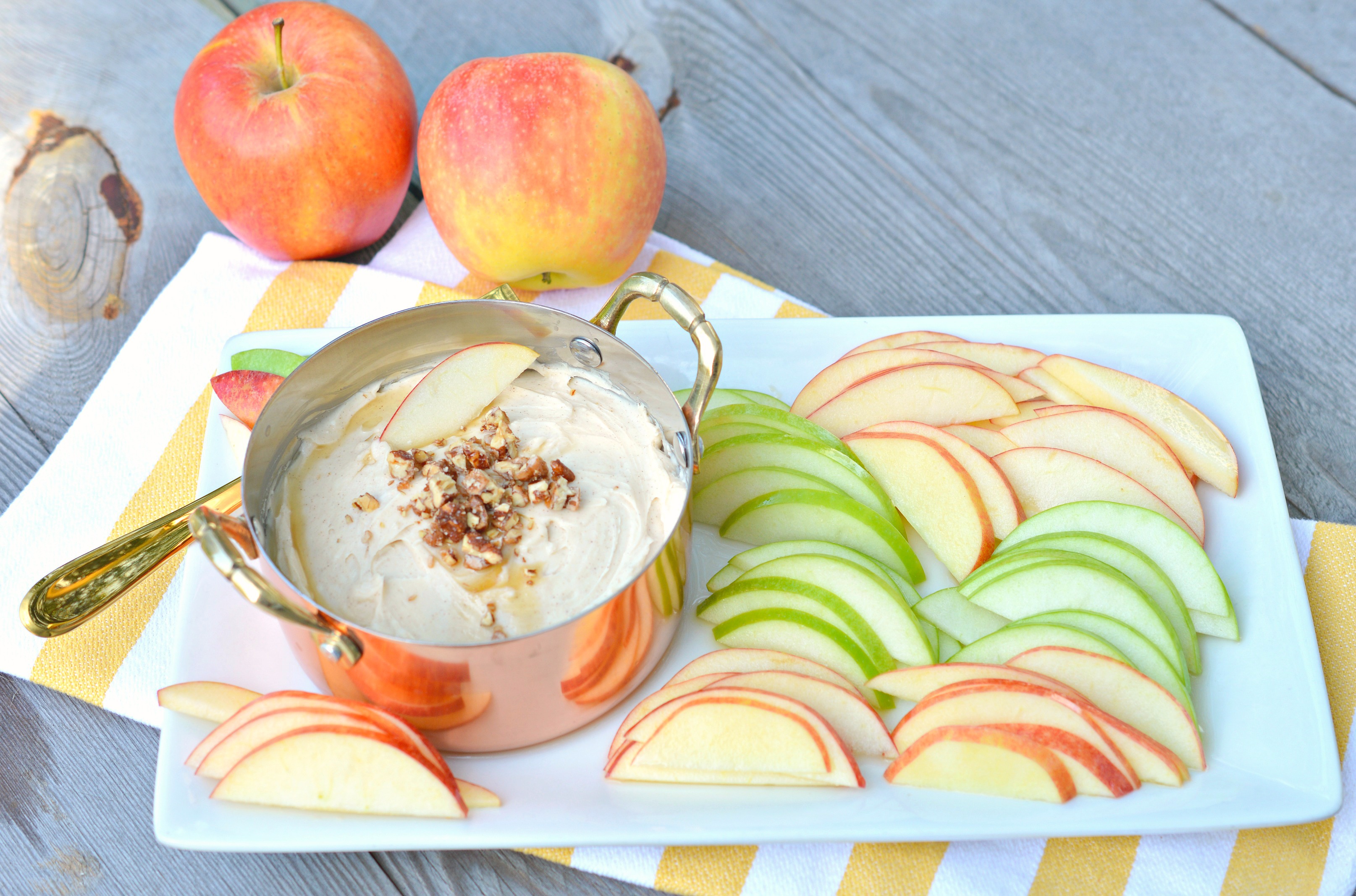 Pan filled with caramel apple cream cheese dip on a white tray and surrounded by green and red apple slices.