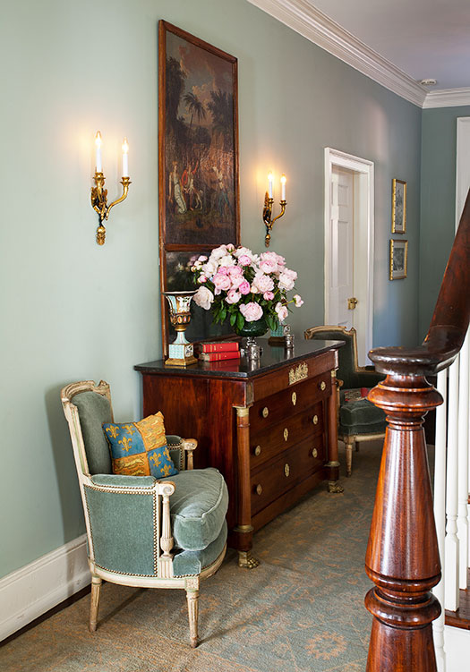 English Country entryway, complete with vintage furniture and a large oil painting flanked by wall sconces.