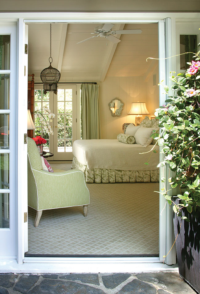 View from a patio in through French doors to a charming cottage bedroom with pastel green and cream accents. 