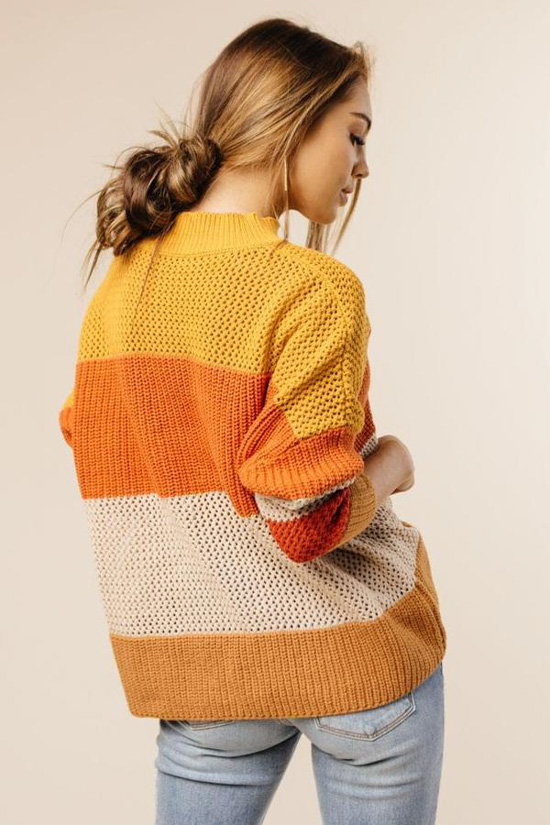 Girl facing away from the camera modeling light denim jeans and a candy corn blocked fall sweater. 