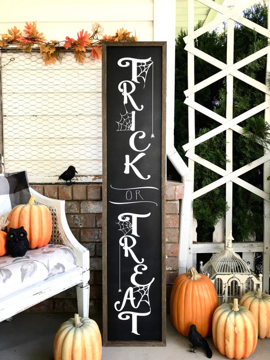 Fall porch accented with various shades and sizes of pumpkins and featuring a large trick or treat wooden sign and other halloween porch decor. 