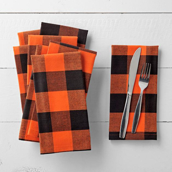 Stack of orange and black buffalo checked cloth napkins and one folded one to the right set with silverware on it. 