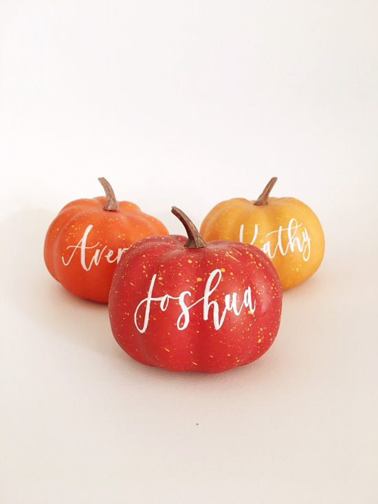 Plastic pumpkins in a variety of colors with hand lettered names written on them as placeholders. 