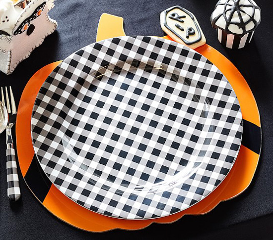 Pumpkin shaped charger topped with a gingham dinner plate next to a gingham handles for and some spooky halloween desserts. 