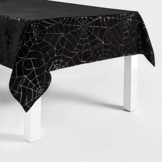 White legged dining table covered in a black tablecloth with metallic silver spider web design. 