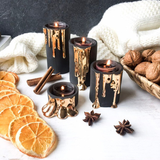 Table setting with various sized black and gold candle holders surrounded by white linens, orange slices and whole walnuts laid out on a table. 