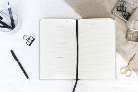 Open journal with black string bookmark, with gray cover surrounded with desk essentials.