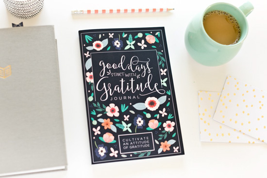 Gratitude journal placed next to a pencil, coffee mug, and notebooks. 