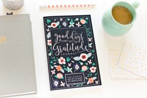 Gratitude journal placed next to a pencil, coffee mug, and notebooks.