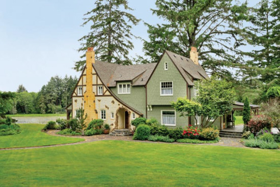 Storybook style cottage in on expansive green grass with mature trees in the background. 