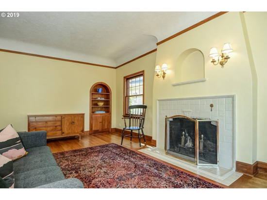 Cottage living room with a Persian rug, gray couch, built in wooden shelving and a white stone fireplace. 