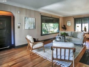 Charming bungalow living room and front door entry with large window letting in light and midcentury modern designed seating around a white rug.