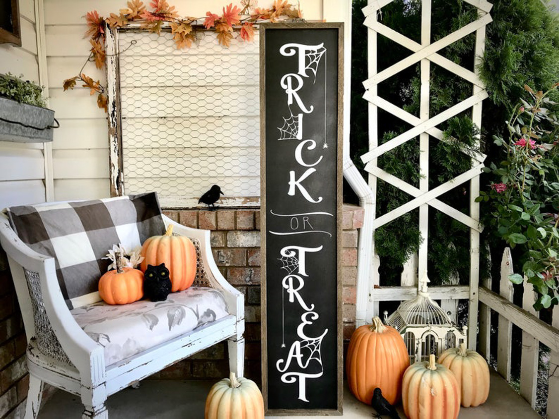 Fall porch accented with various shades and sizes of pumpkins and featuring a large trick or treat wooden sign.