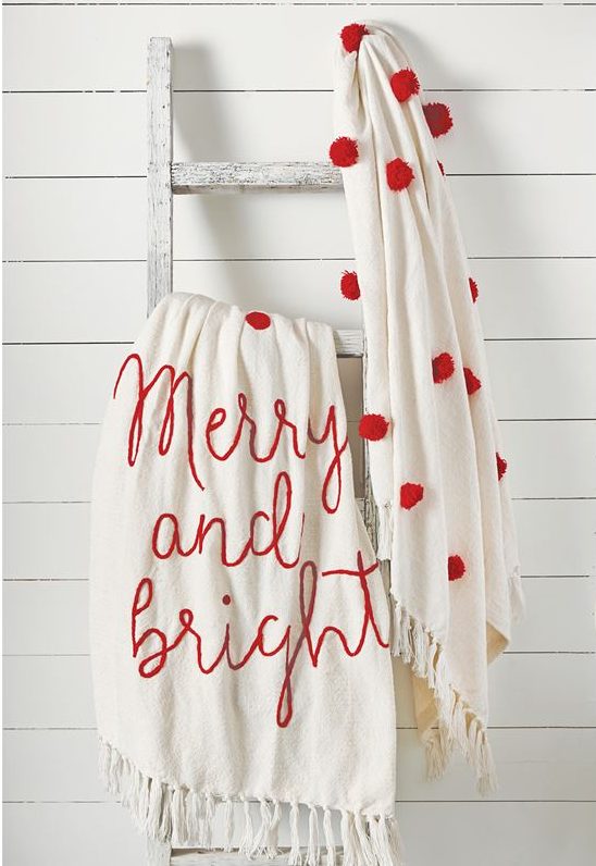 merry and bright throw blanket and red and white pom pom throw on a ladder.