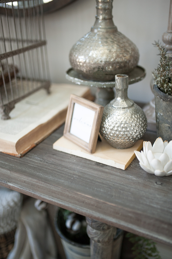 Entryway table topped with small trinkets like metal vases, porcelain lotus flowers and a fresh plant. 