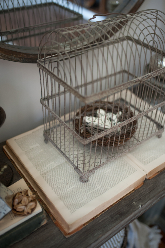 An vintage book laying open on an entryway table and topped with an antique birdhouse filled with a faux nest. 