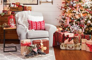 A cozy light colored armchair sat next to a sparkly lit Christmas tree surrounded by gifts.