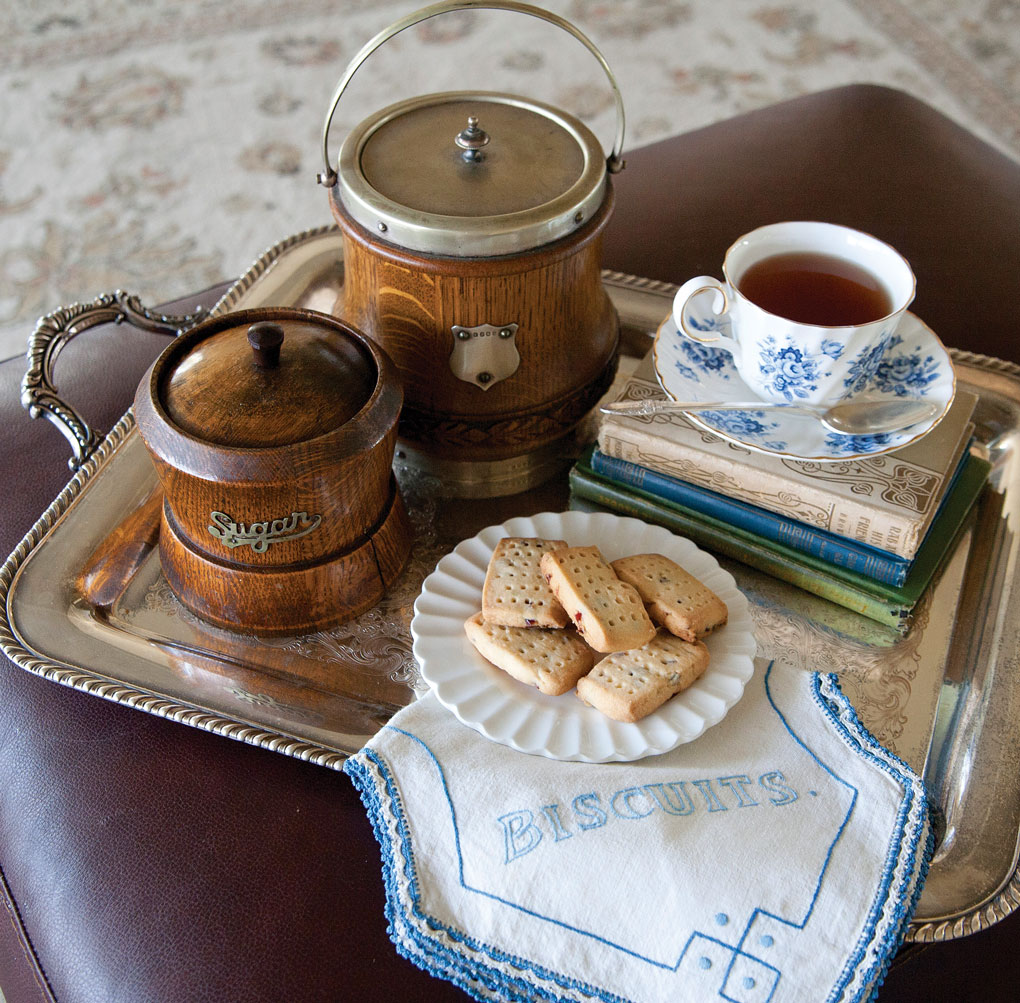 Antique wooden tea and sugar containers set out on a silver tray with tea and biscuits. 