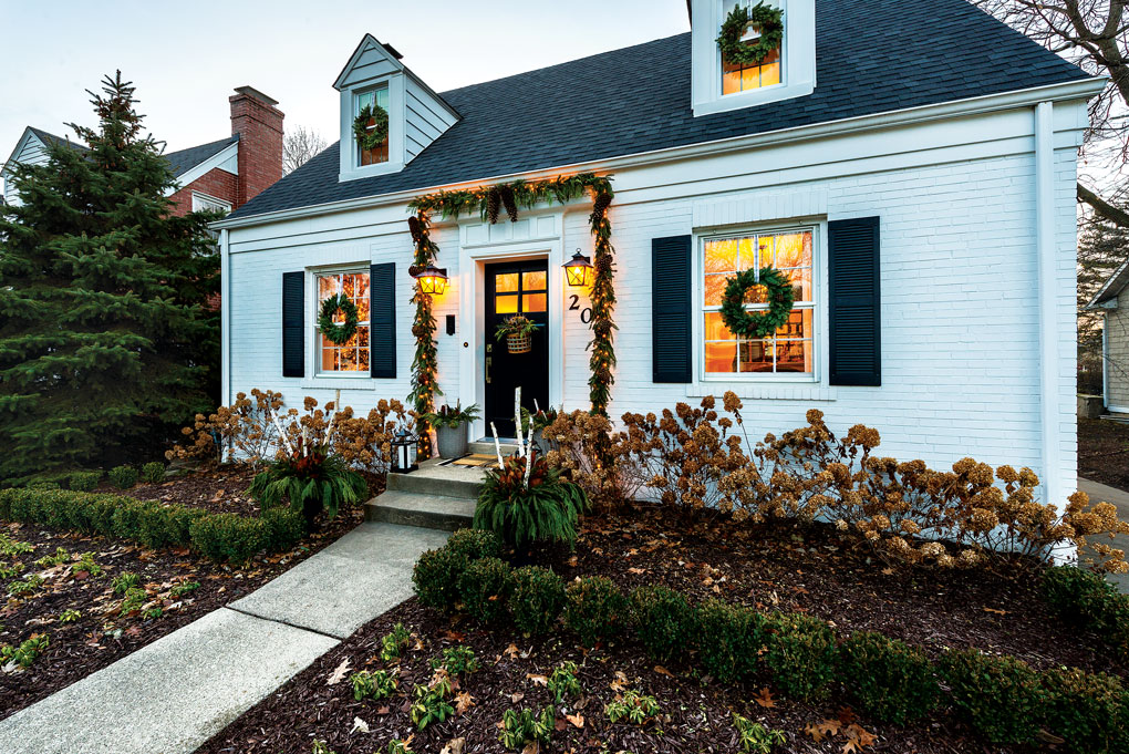 Charming cape cod styled home with a dormers and Christmas wreaths hanging on the front door and in front of each window. 