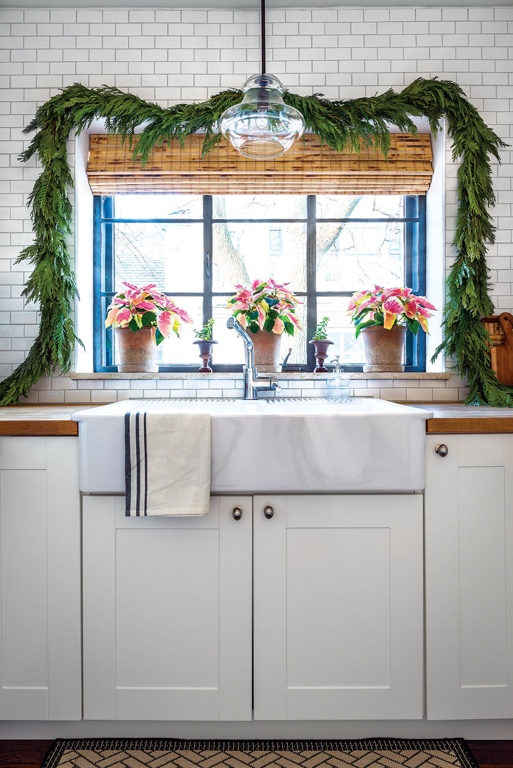 Modern farmhouse styled kitchen in white with bamboo window coverings and Christmas greenery over the window with poinsettia accents. 