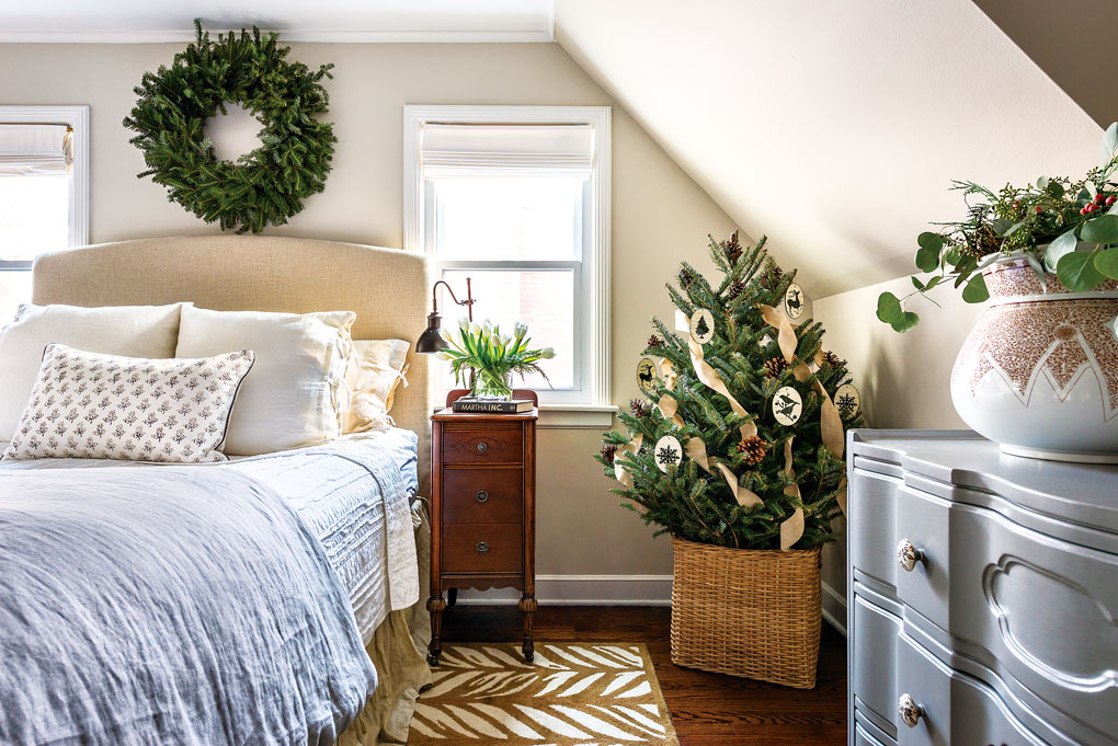 Light and bright bedroom with a mini Christmas tree in the corner and a wreath placed above the bed. 