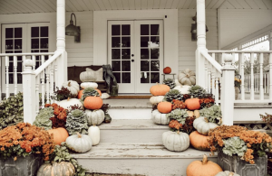White farmhouse front porch steps covered in varied size and colored pumpkins and fall florals.
