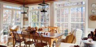 Lake house dining room with pine farm table and hanging lantern pendants overhead surrounded by a wall of windows.