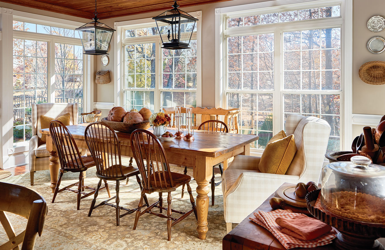 Lake house dining room with pine farm table and hanging lantern pendants overhead surrounded by a wall of windows.