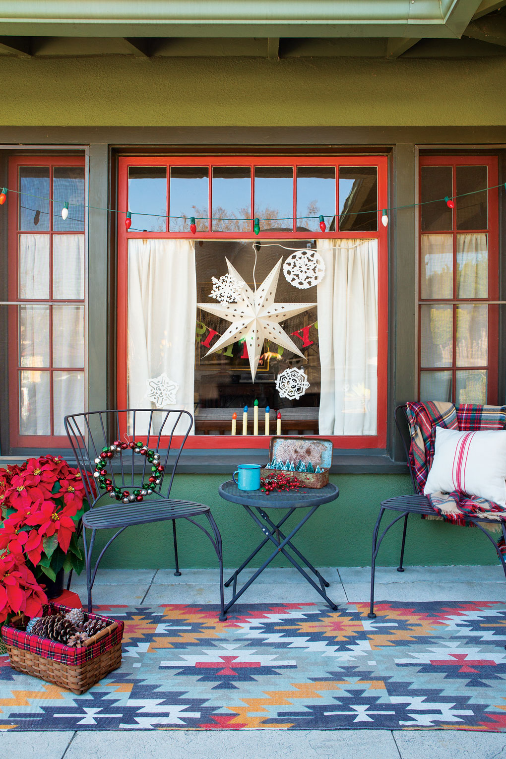 Metal black bistro set sitting on the front porch atop a Navajo inspired rug flanked by poinsettias. 