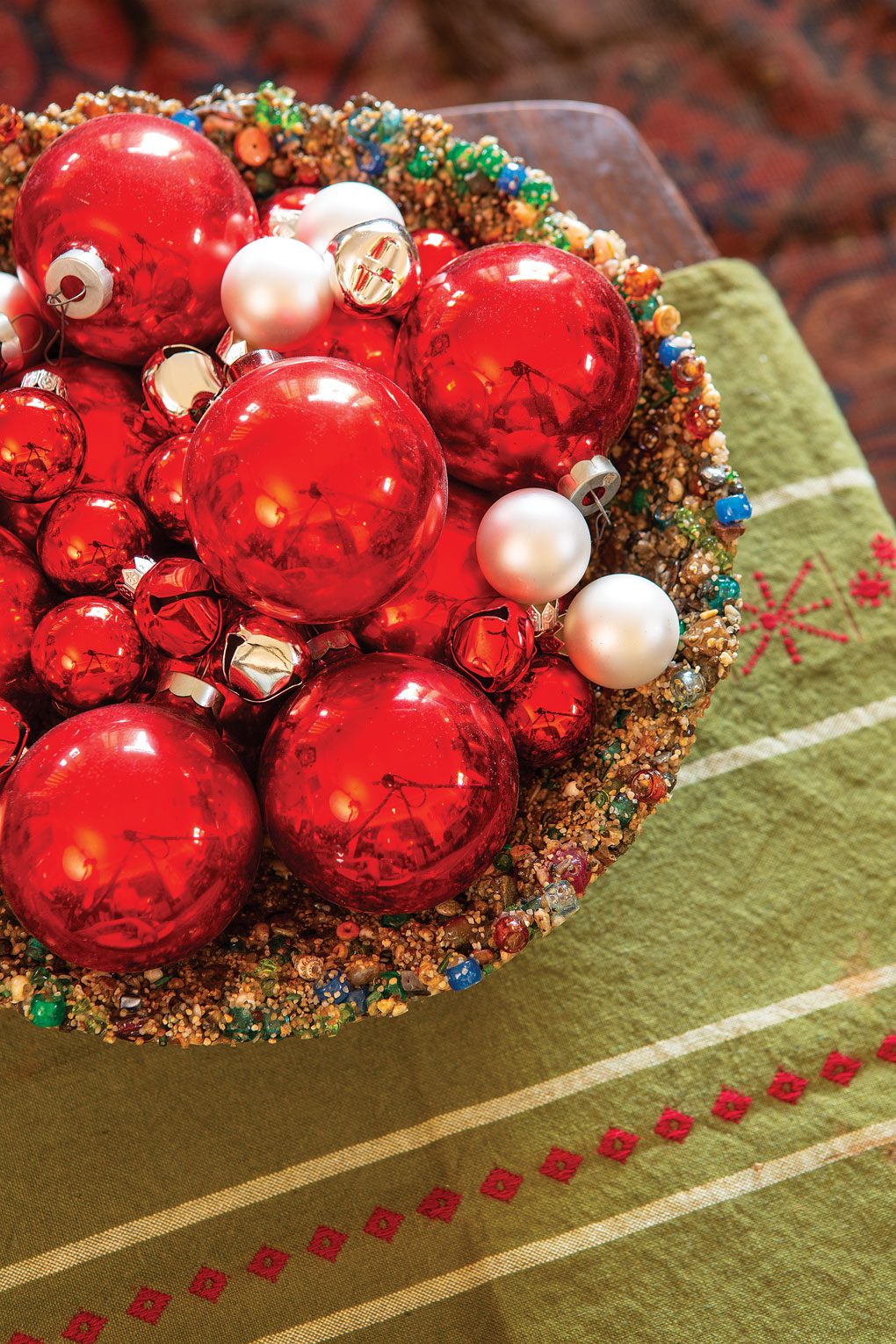 Vintage holiday table runner topped with a large centerpiece bowl filled with glass antique red ball ornaments. 