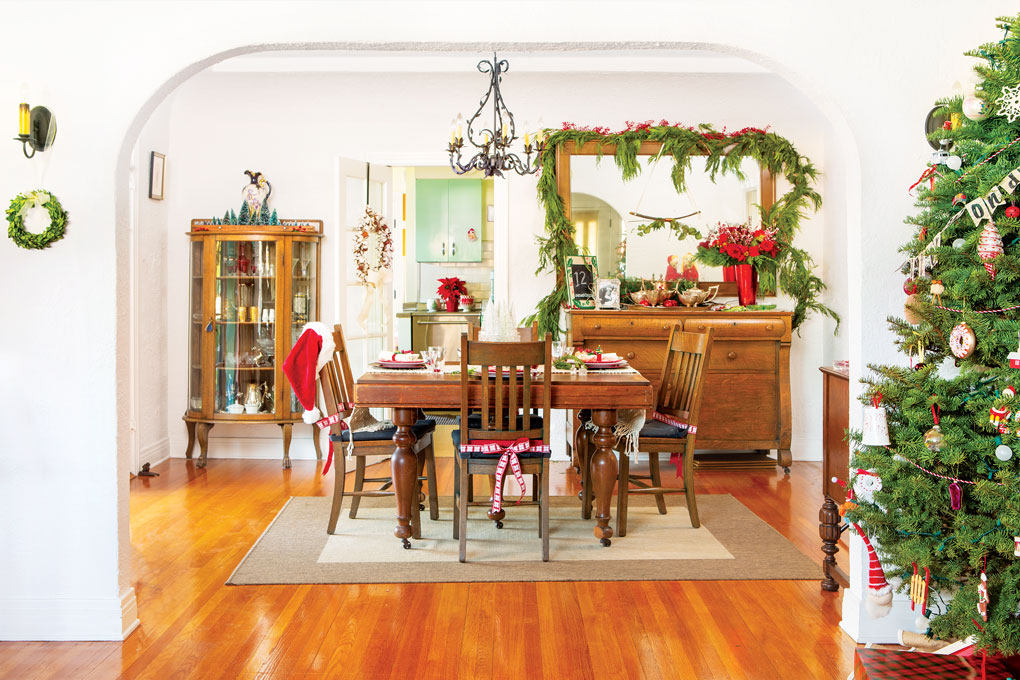 A curved arch looking through to a Christmas decorated dining room filled with antique wood furniture. 