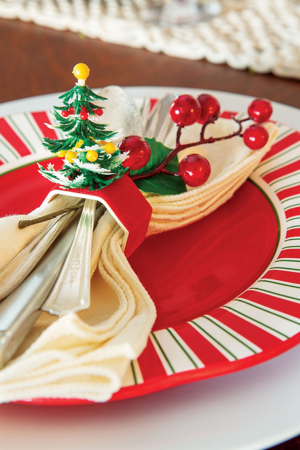 Holiday dinner place setting topped with a cream napkin and vintage napkin ring topped with a Christmas tree. 