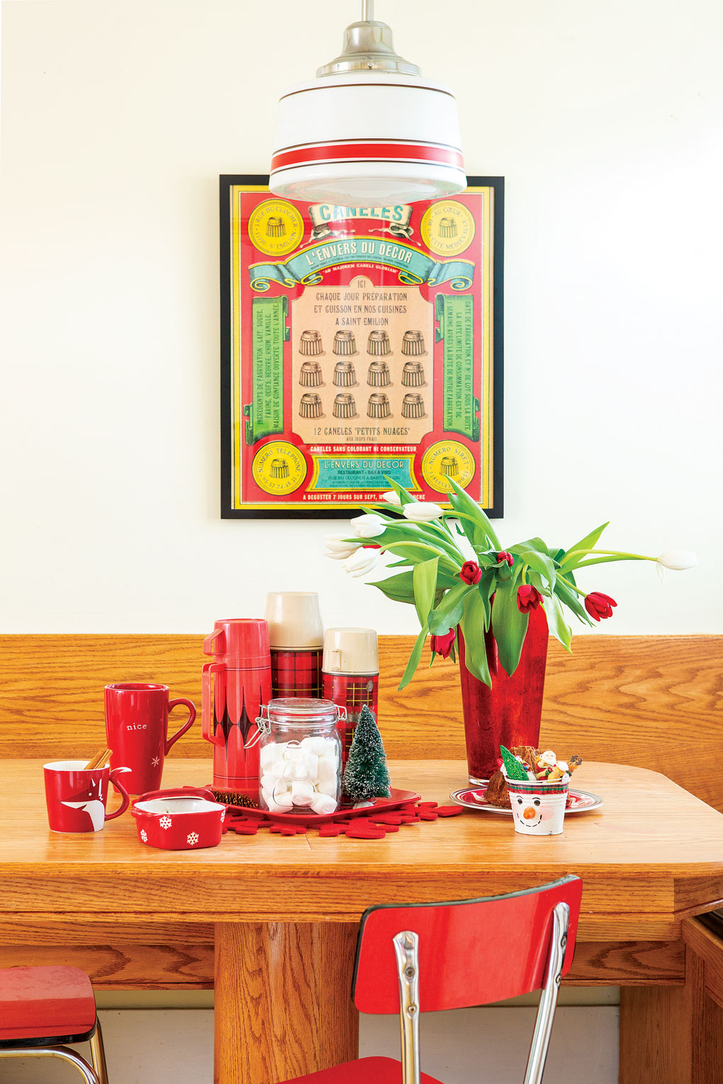 A wooden breakfast nook is adorned with red accents, a vase of red tulips and a collection of vintage thermoses. 