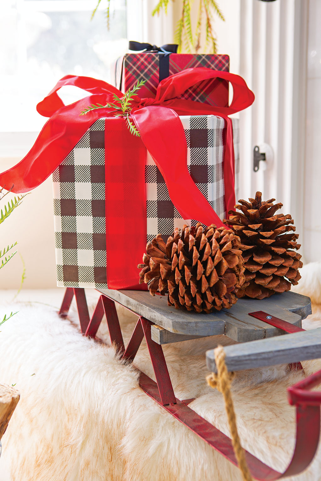 Pinecones and a black and white gingham wrapped present with a red bow sit on an indoor decorative sled for a rustic Christmas look.