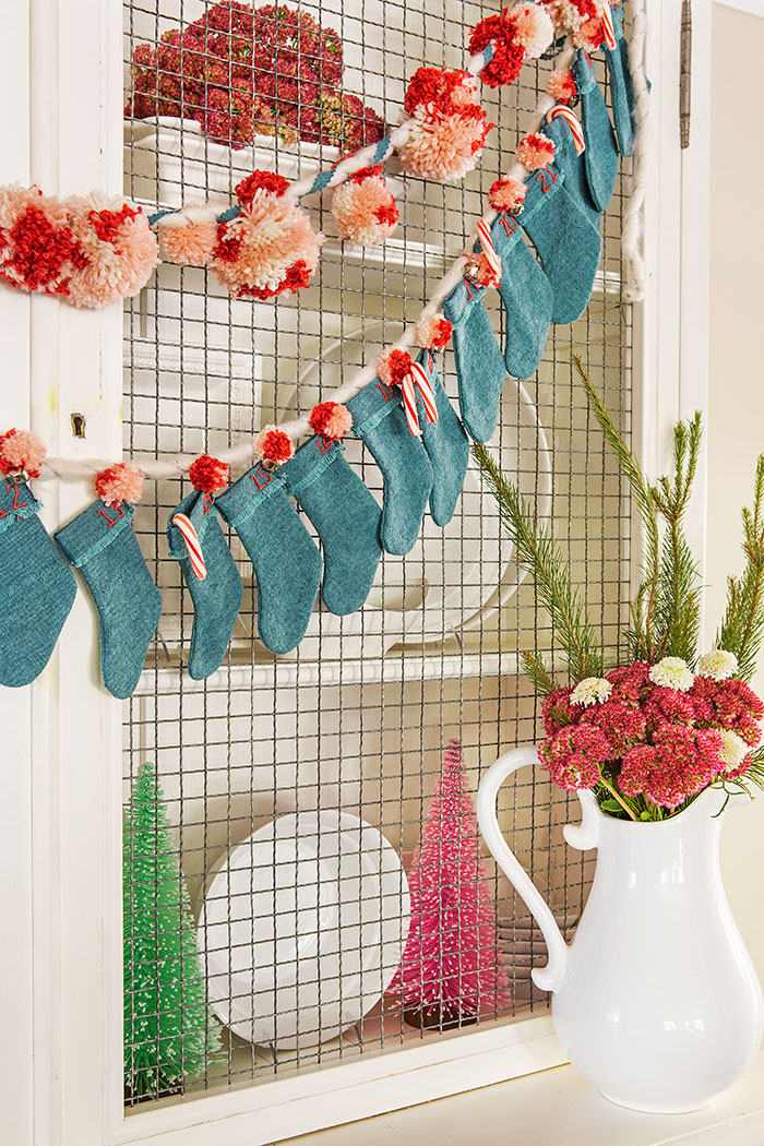 Mini stocking advent calendar hung on the front of a white cabinet filled with white dishes and pink flowers