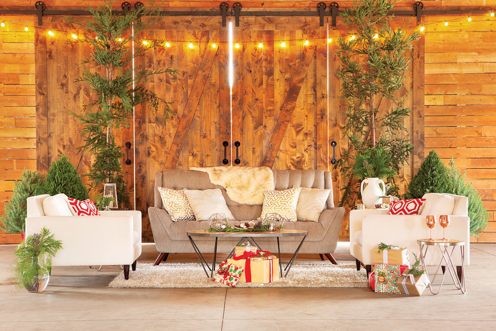 Christmas entertaining area made in a barn, flanked with miniature pines and sprinkled with gifts and pops of red. 