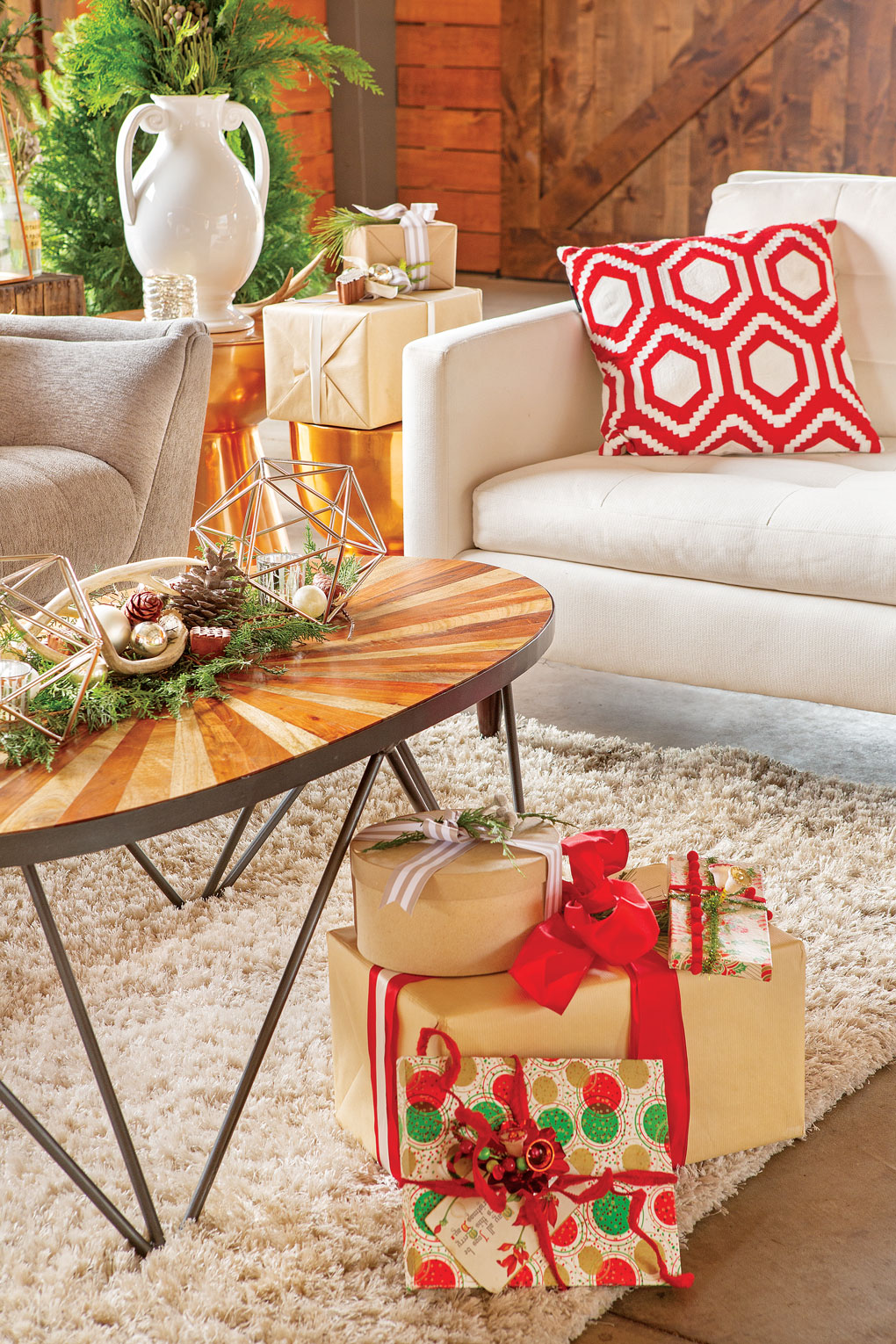 Sitting area with a light colored couch and armchair in the background and a midcentury inspired coffee table with a pile of wrapped Christmas gifts in the foreground.