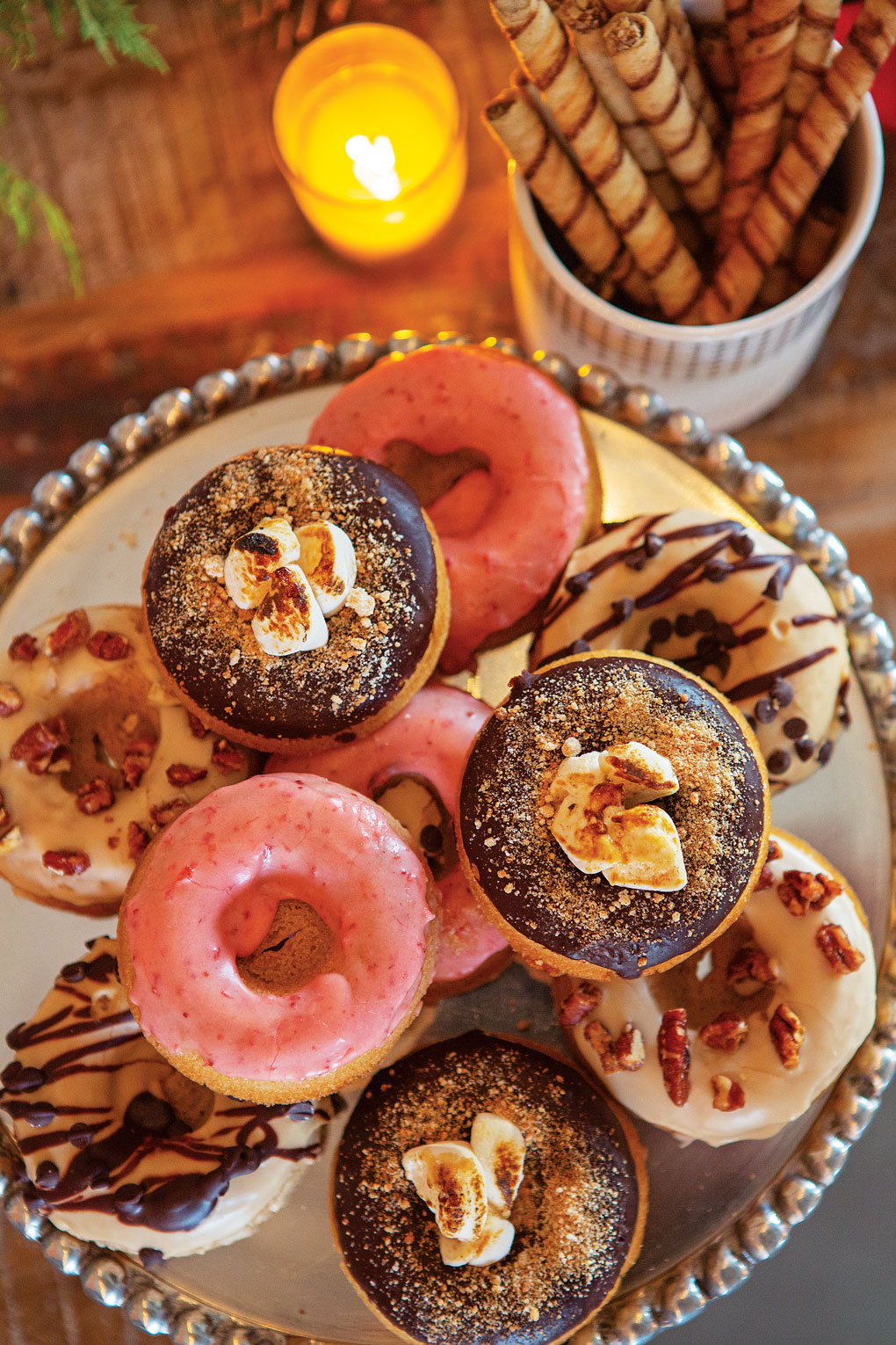 Aerial view of a silver tray of gourmet donuts next to desserts and a lit votive candle. 