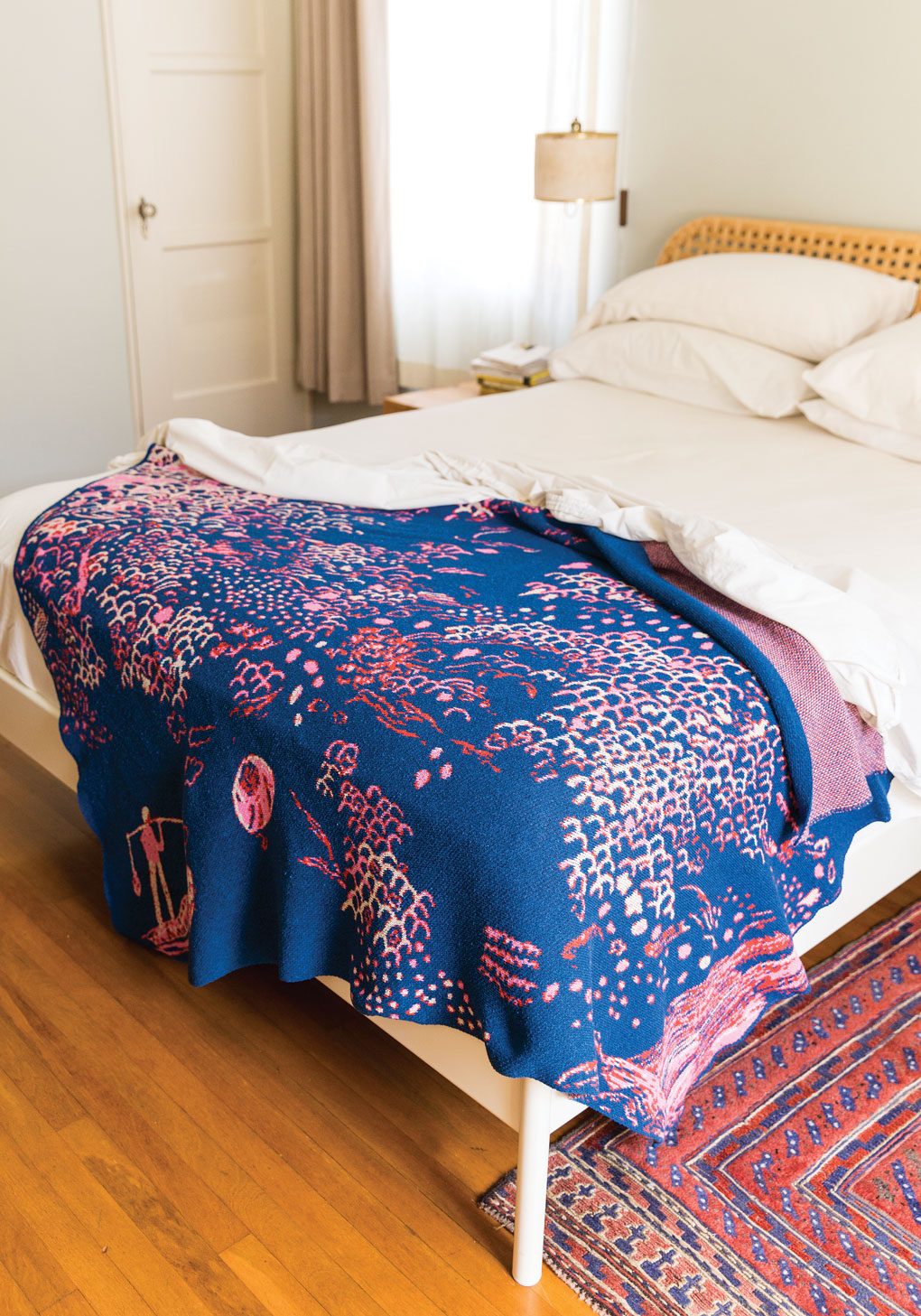 Rattan bed frame with cozy white bedding featuring a bold royal blue blanket with rose colored accents. 