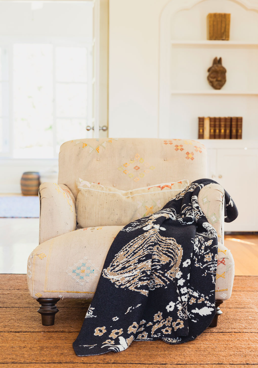 Antique looking armchair featuring a bold printed throw blanket resting over the arm. 