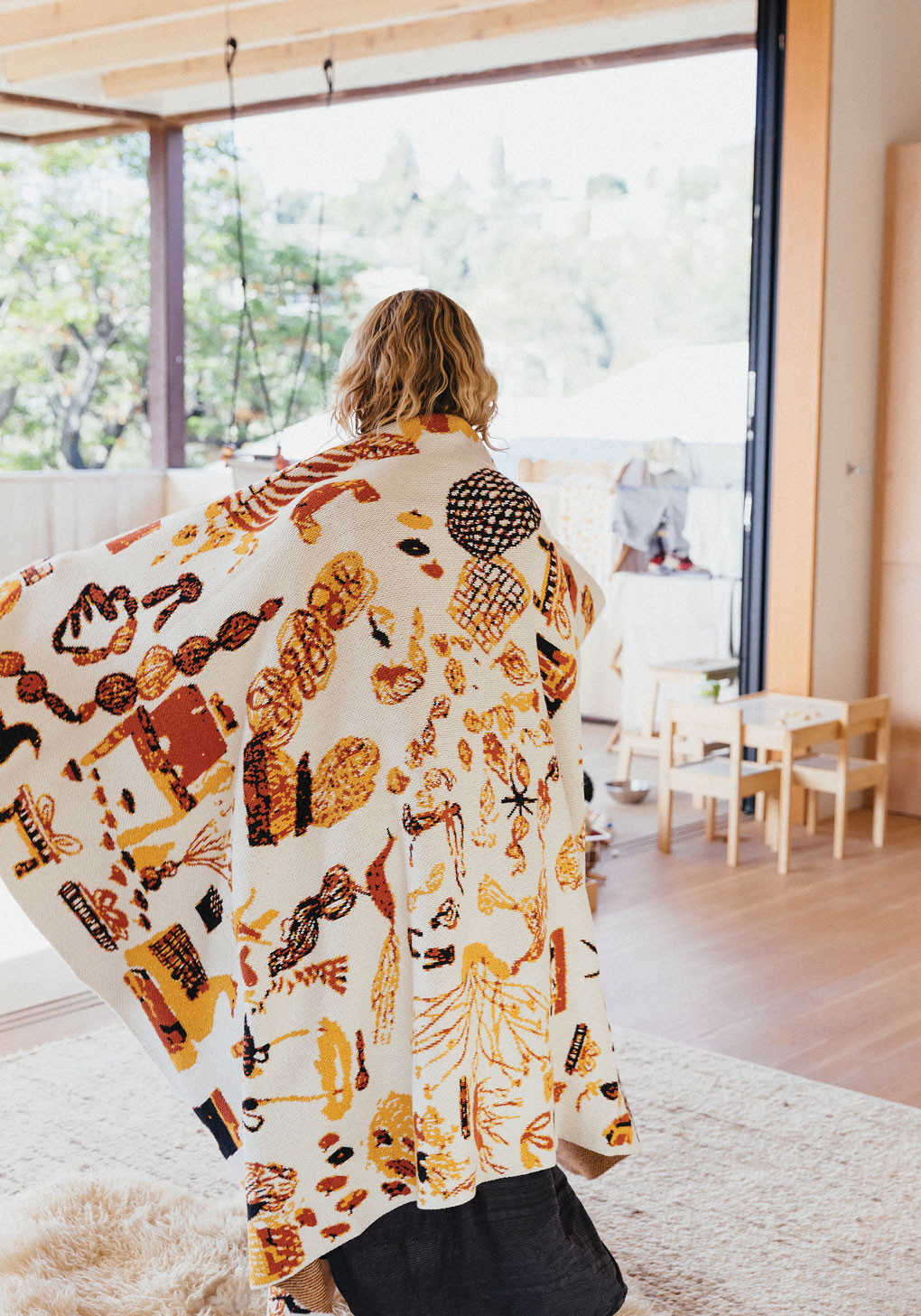 Open and modern living space with a girl twirling in sunlight and modeling a vibrant blanket. 