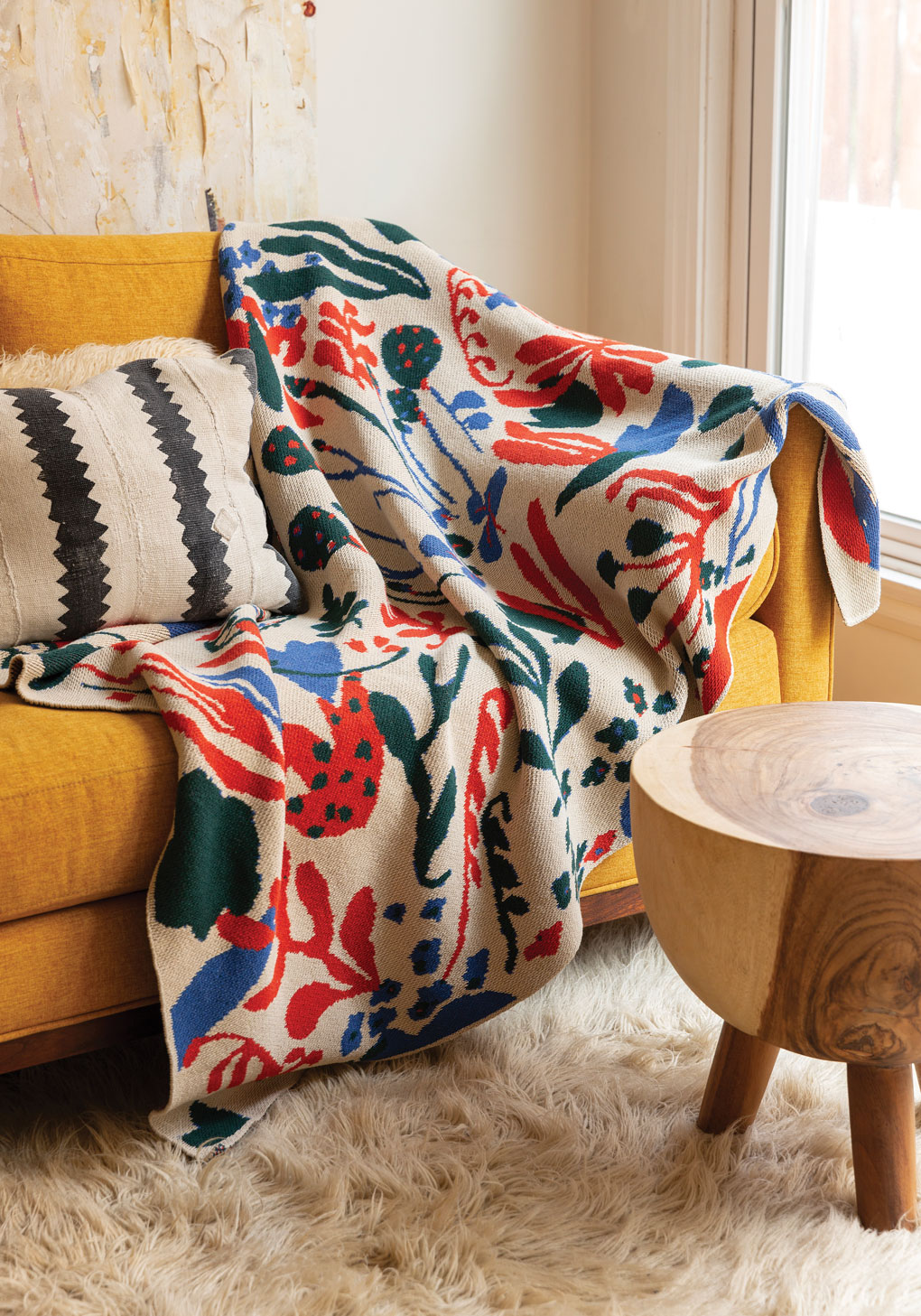 Mustard colored couch with a colorful and bold throw blanket draped over the arm. 